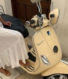 a woman in white dress sitting on a yellow scooter next to a building