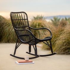 a rocking chair sitting on top of a cement ground next to tall grass and plants