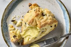 a scone with butter and raisins is on a plate next to a fork