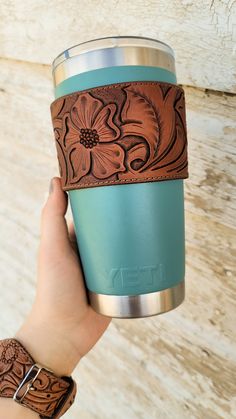 a person holding a cup with a flower design on the side and brown leather band around it