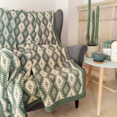 a green and white blanket sitting on top of a chair next to a potted cactus