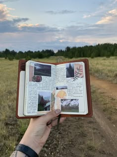 a person holding an open book in their hand on a dirt road with grass and trees