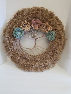 a wreath made out of yarn with flowers on top and beads around the edges, hanging from a white wall