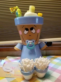 a baby doll sitting on top of a table next to two cups filled with toothbrushes