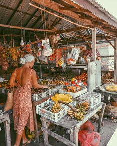 a woman standing in front of a fruit stand with bananas and other fruits on it