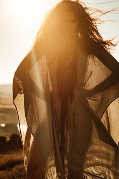 a woman standing on top of a sandy beach next to the ocean with her hair blowing in the wind