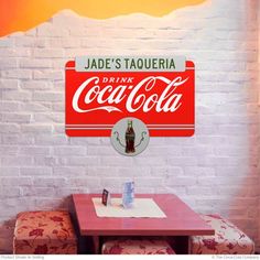 there is a coca - cola sign on the wall above a table and two chairs