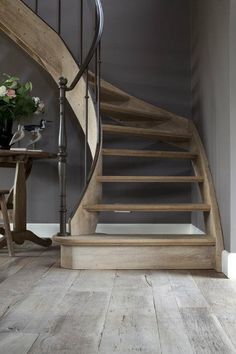 a wooden stair case next to a table with flowers on it in front of a gray wall