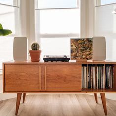 a record player sitting on top of a wooden cabinet next to a window with potted plants