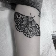 a black and white photo of a moth tattoo on the right thigh, with an eyeball in the middle