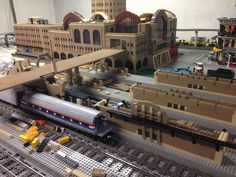 a toy train is on the tracks in front of a model city with buildings and trains