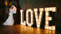 a bride and groom standing in front of the word love lit up at their wedding