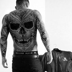 a man with tattoos standing in front of a luggage bag and looking at his back