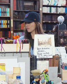 a woman standing in front of a book shelf filled with lots of books and other items