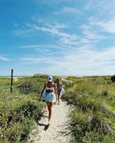 two women in bathing suits walking down a path to the beach on a sunny day