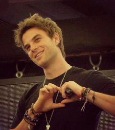 a young man making a heart with his hands and smiling at the camera while standing in front of a screen