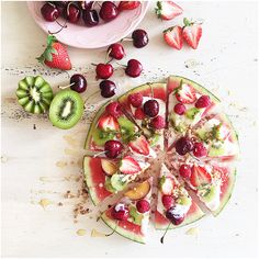 a watermelon and kiwi fruit pizza on a plate with sliced strawberries