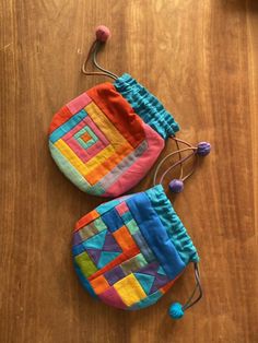 two small colorful bags sitting on top of a wooden table next to a sewing needle