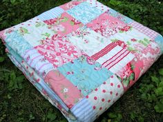 a patchwork quilt on the ground with grass and bushes in the backround