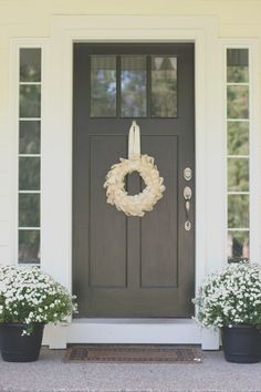 two black pots with white flowers and a wreath on the front door to a house