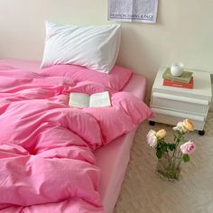 a bed with pink sheets and pillows next to a vase filled with flowers on the floor