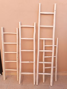 three wooden ladders sitting next to each other on top of a tile floor in front of a pink wall