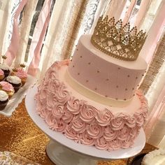 a pink and gold wedding cake with cupcakes on the table next to it