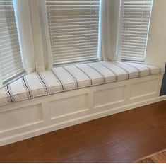 a window seat in front of two windows with white blinds and wood flooring on either side