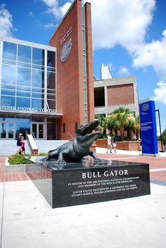 a statue of a gator in front of a building with people walking around it