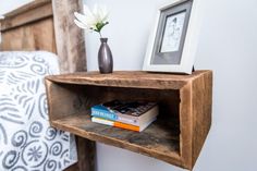 a wooden shelf with two books on it next to a bed and a framed photo