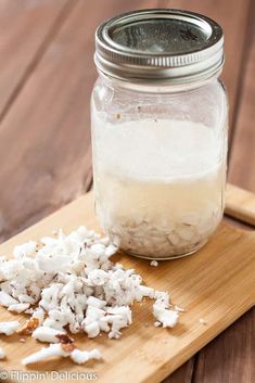 a wooden cutting board topped with a glass jar filled with white rice next to a spoon