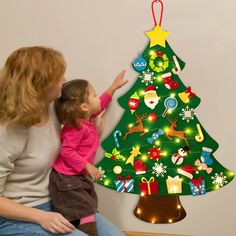 a woman and her child are sitting in front of a christmas tree that has lights on it