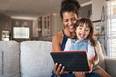 a woman sitting on a couch holding a child and looking at an electronic device in front of her