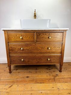 an old wooden dresser with a white sink on it's top and wood floors