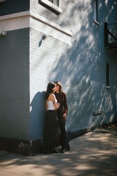 two people standing next to each other in front of a blue building with a shadow on the wall