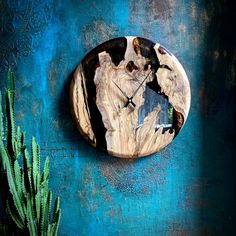 a clock that is on the side of a blue wall next to a cactus plant