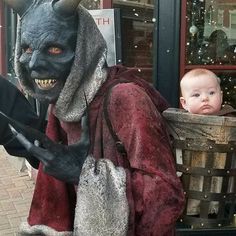 a man dressed as a demon with a baby in his arms and wearing a costume