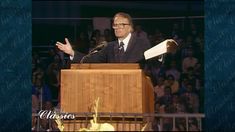 a man standing at a podium in front of a crowd with his hands out to the side