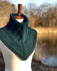 a white mannequin wearing a green knitted shawl on top of a body of water