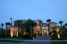 a large house with palm trees and lights on the front yard at night in florida