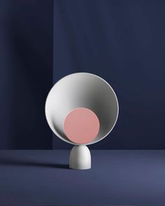 a white and pink vase sitting on top of a blue table next to a black wall