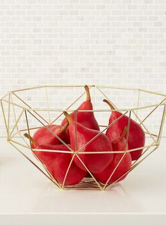 a wire basket filled with red fruit sitting on top of a table next to a wooden block