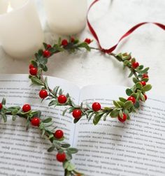 an open book with holly and red berries on it next to two white votive candles