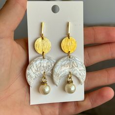 a pair of white and gold earrings with pearls on the bottom are being held in front of a card