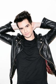 a young man wearing a black shirt and leather jacket with his hands on his head