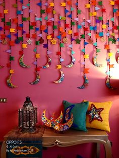 colorful paper stars and crescents hang on the wall above a table with a lamp