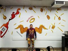 a man standing in front of a wall with food drawings on it and an advertisement for krispy kreme