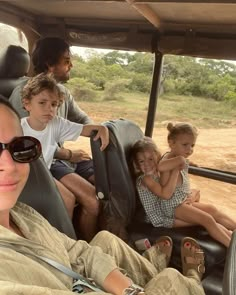 a group of people riding in the back of a vehicle on a dirt road next to trees