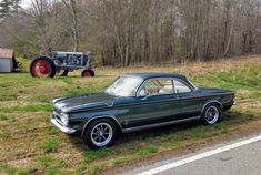 an old car is parked on the side of the road next to a farm tractor