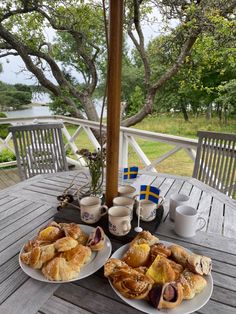 two plates with pastries on them sitting on a wooden table near trees and water